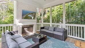 A covered outdoor seating area with wicker furniture, a flat-screen TV, and a fireplace. - Liv'n the Good Life sleeps 11 (St Simons Island)