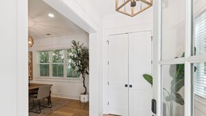 A spacious room with a wooden floor, a dining area with a table and chairs, a potted plant, and a white door with a keypad lock. - Liv'n the Good Life sleeps 11 (St Simons Island)