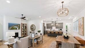 A spacious living room with a fireplace, a dining area with a wooden table and chairs, and a kitchen with modern appliances. - Liv'n the Good Life sleeps 11 (St Simons Island)