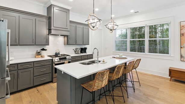 A modern kitchen with grey cabinets, a white island, and bar stools. - Liv'n the Good Life sleeps 11 (St Simons Island)