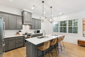 A modern kitchen with grey cabinets, a white island, and bar stools. - Liv'n the Good Life sleeps 11 (St Simons Island)