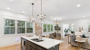 A spacious kitchen with a large island, modern pendant lights, and a dining area with a sofa and table. - Liv'n the Good Life sleeps 11 (St Simons Island)
