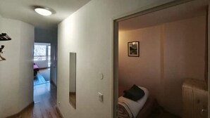 Passadís estret amb un paviment de fusta que condueix a una habitació amb un llit i una petita finestra.