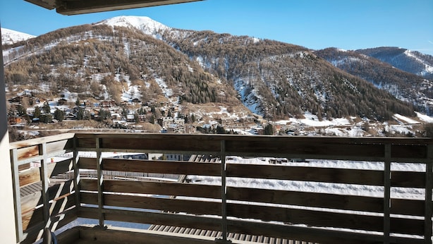 Un balcó amb vista a un paisatge de muntanya, amb vessants cobertes de neu i un poble a la valla.