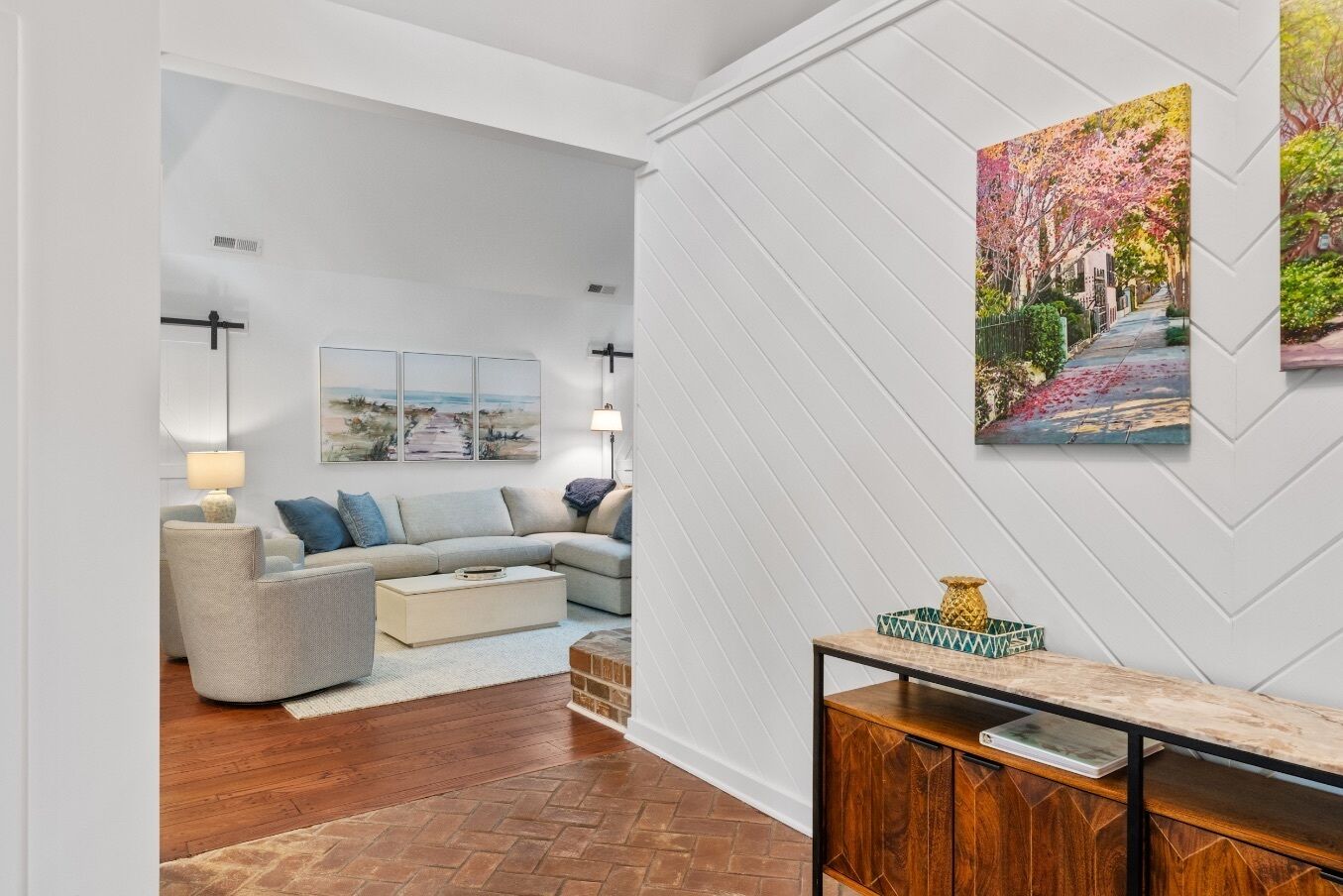 A modern living room with a sectional sofa, a coffee table, a wooden herringbone floor, and a console table with decorative items.