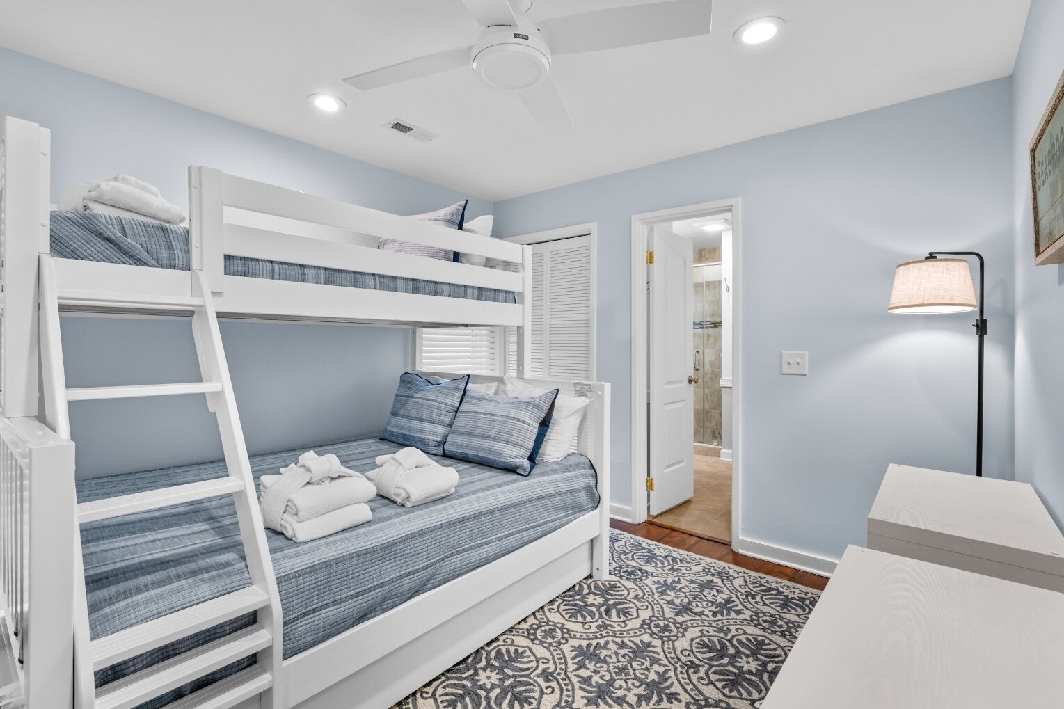 A bunk bed room with a ceiling fan, a patterned rug, and a bedside lamp.