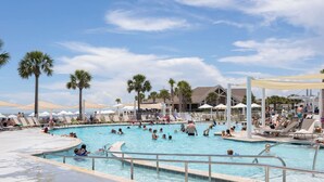 Una gran piscina al aire libre con varias pistas, rodeada de palmeras y sombrillas.