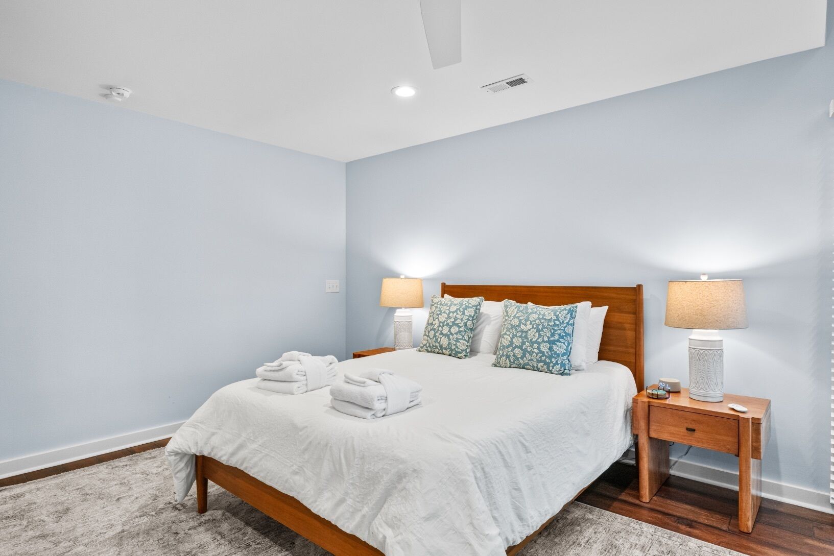 Une chambre à coucher comprenant un lit, deux tables de chevet, une commode, une lampe et un luminaire fixé au mur.