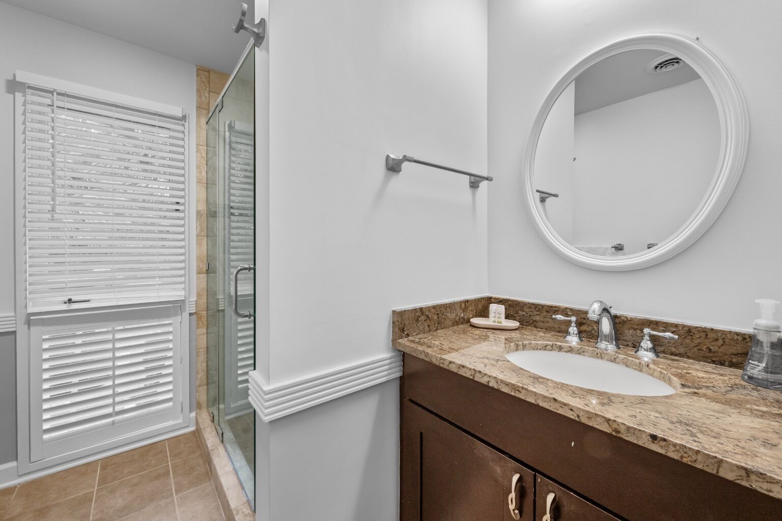 A bathroom with two sinks, a round mirror, and a glass shower enclosure.