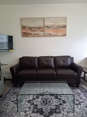 A living room with a dark brown sofa, a glass coffee table with a patterned rug, and two abstract paintings on the wall. - Millionaire stay - steps to the beach -very comfortable and peaceful - Enjoy (Surfside)