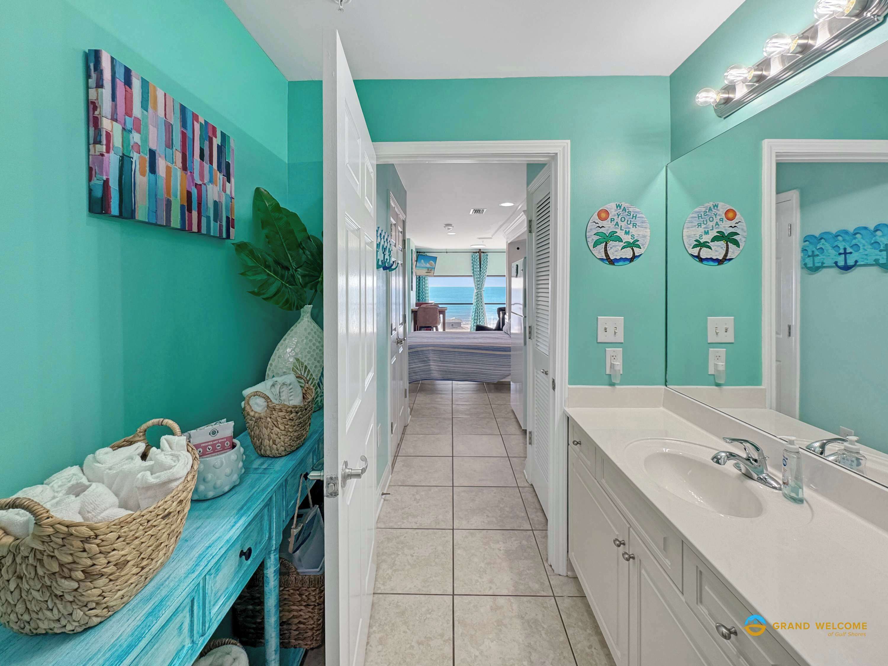 A bathroom with a large mirror, a sink, and a shower area. There is a door leading to a bedroom with a view of the ocean.