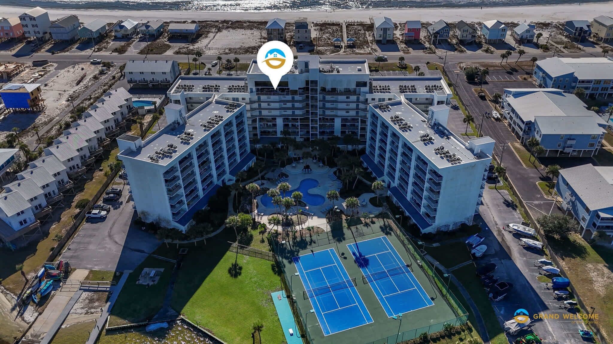 A multi-story hotel with a central courtyard, parking, and a tennis court.