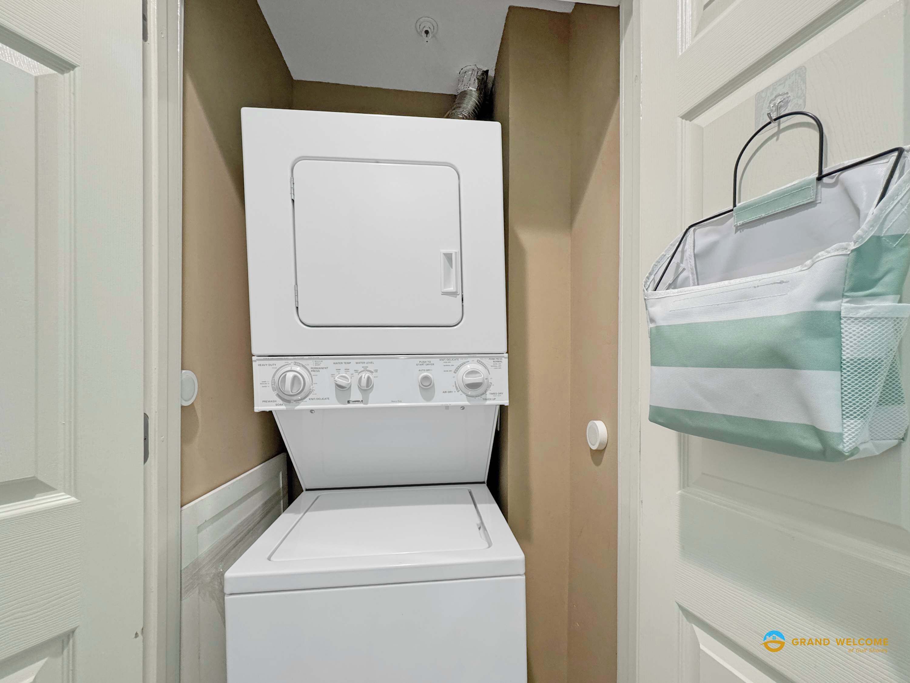 A compact laundry room with a front-loading washer and dryer, a towel rack, and a door with a towel hanging on it.