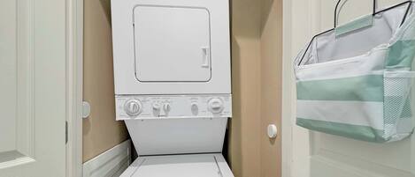 A compact laundry room with a front-loading washer and dryer, a towel rack, and a door with a towel hanging on it.