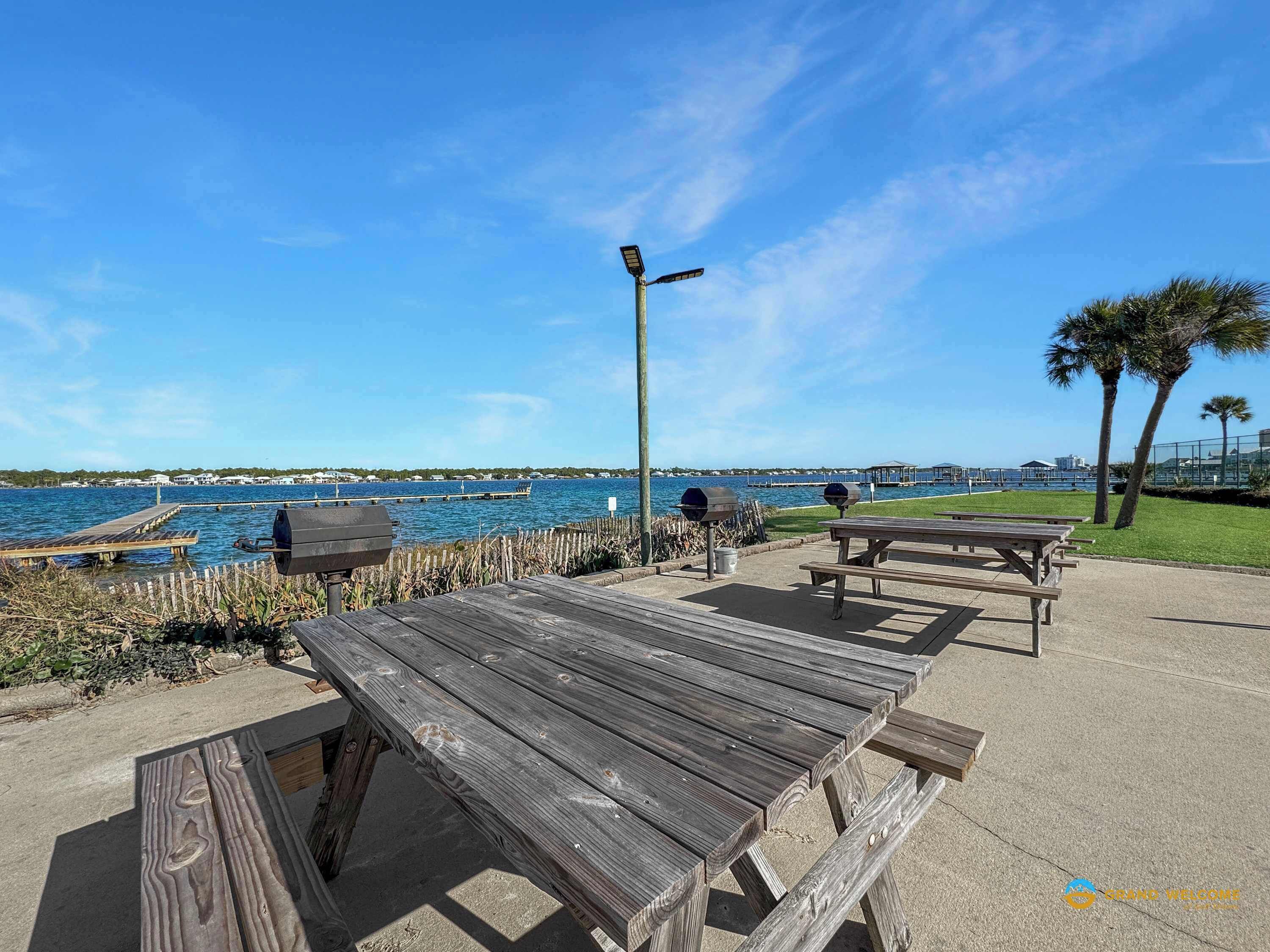 A wooden deck with picnic tables and barbecue grills overlooking a body of water.