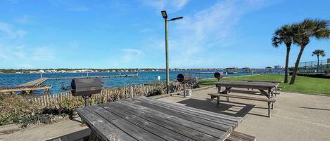 A wooden deck with picnic tables and barbecue grills overlooking a body of water.