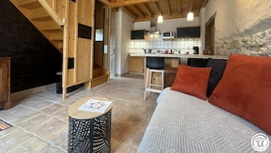 A cozy interior with a wooden staircase, a kitchen area, and a living space with a sofa and cushions. - Grange Carrée (Saint-Rémy)