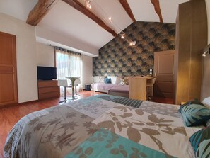 A bedroom with a large bed, a desk, a chair, a TV, and a window with curtains. - Grange Carrée (Saint-Rémy)