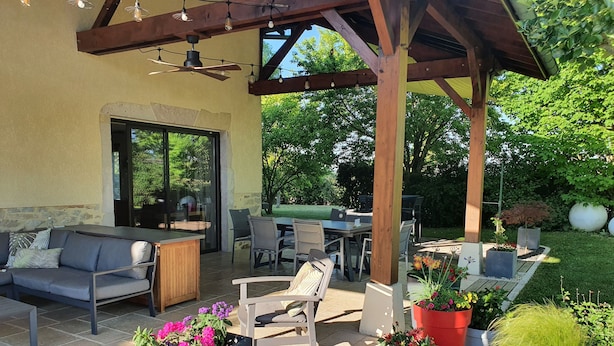An outdoor patio with a wooden pergola, seating area, and planters with flowers. - Grange Carrée (Saint-Rémy)
