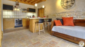 A cozy kitchen with wooden cabinets, a central island, and a stone wall. - Grange Carrée (Saint-Rémy)
