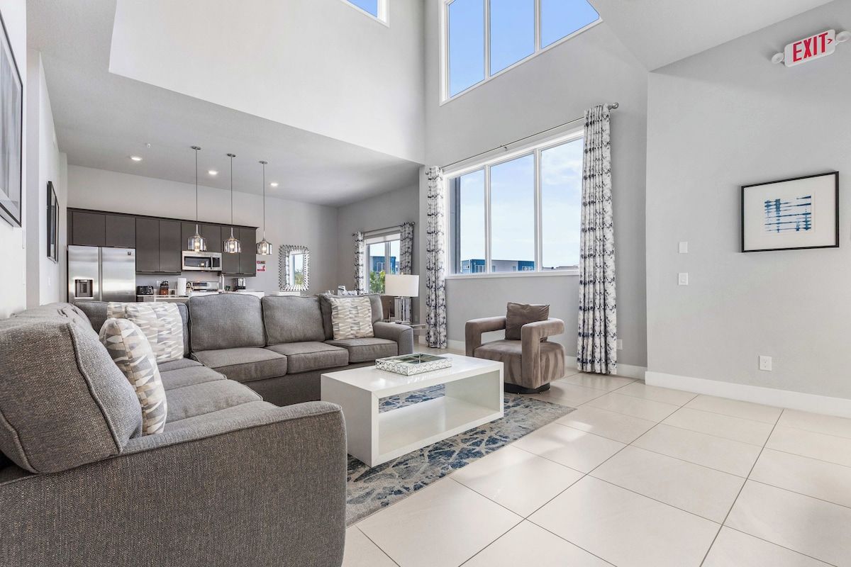 A modern living room with a sectional sofa, a white coffee table, and a view of the kitchen.