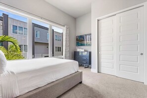 A bedroom with a bed, a dresser, a painting, and a view of neighboring buildings. - Sleeps 10•Private balcony dining•Near Disney (Kissimmee)