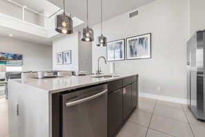 A modern kitchen with a central island, stainless steel appliances, pendant lighting, and artwork on the walls. - Sleeps 10•Private balcony dining•Near Disney (Kissimmee)