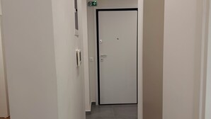 A narrow, well-lit hallway with a tiled floor, a door at the end, and a small window on the left wall. - Core Stay Marousi Fully Renovated Studio (Marousi)