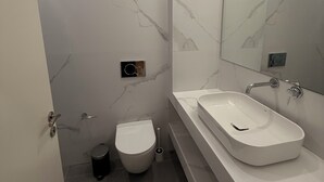 A modern bathroom with a white marble wall, a large mirror, a white sink, and a toilet. - Core Stay Marousi Fully Renovated Studio (Marousi)