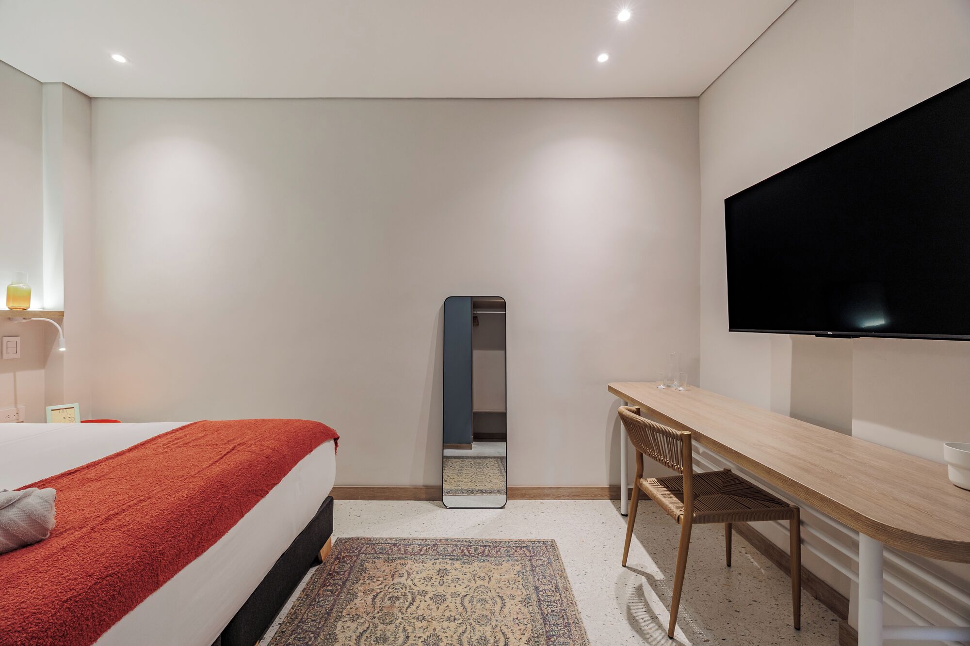 Een moderne hotelkamer met een bed, een bureau, een spiegel en een televisie.