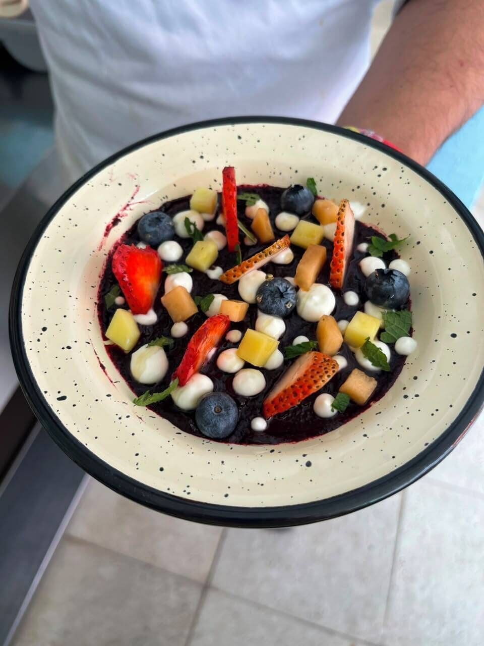 Una ciotola di insalata di frutta con diverse bacche, noci e un condimento cremoso.