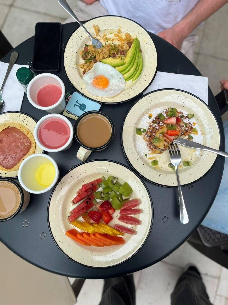 A table with various breakfast dishes, including eggs, avocado, and fruit.