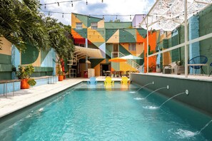 Una piscina con sillas coloridas, un área de estar cubierta y un edificio con diseños geométricos.