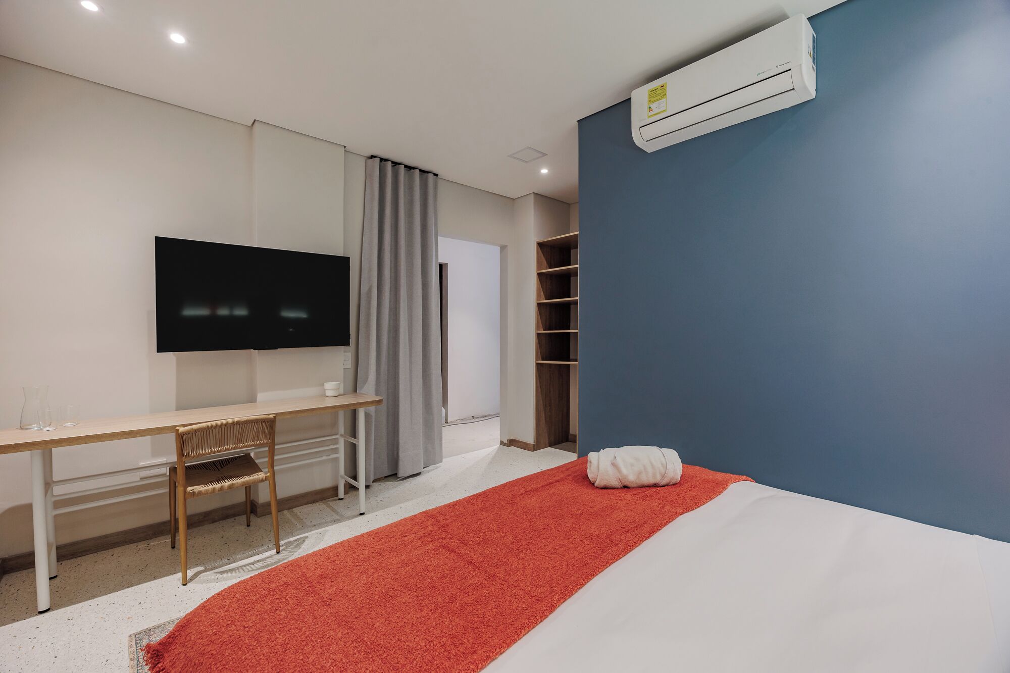 Ett modernt hotellrum med en säng, ett skrivbord, en tv och en luftkonditioneringsanläggning.