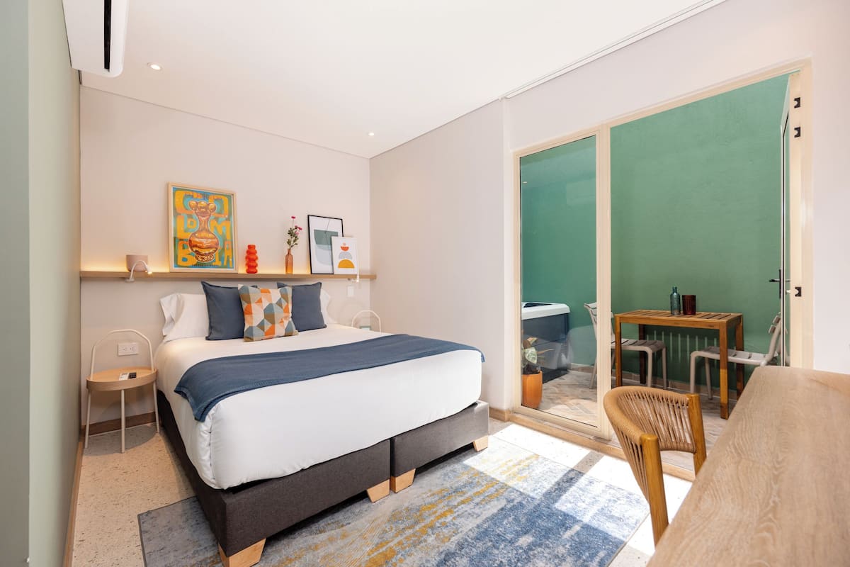 Quarto moderno com cama, mesas de cabeceira, uma cadeira e vista para o exterior.