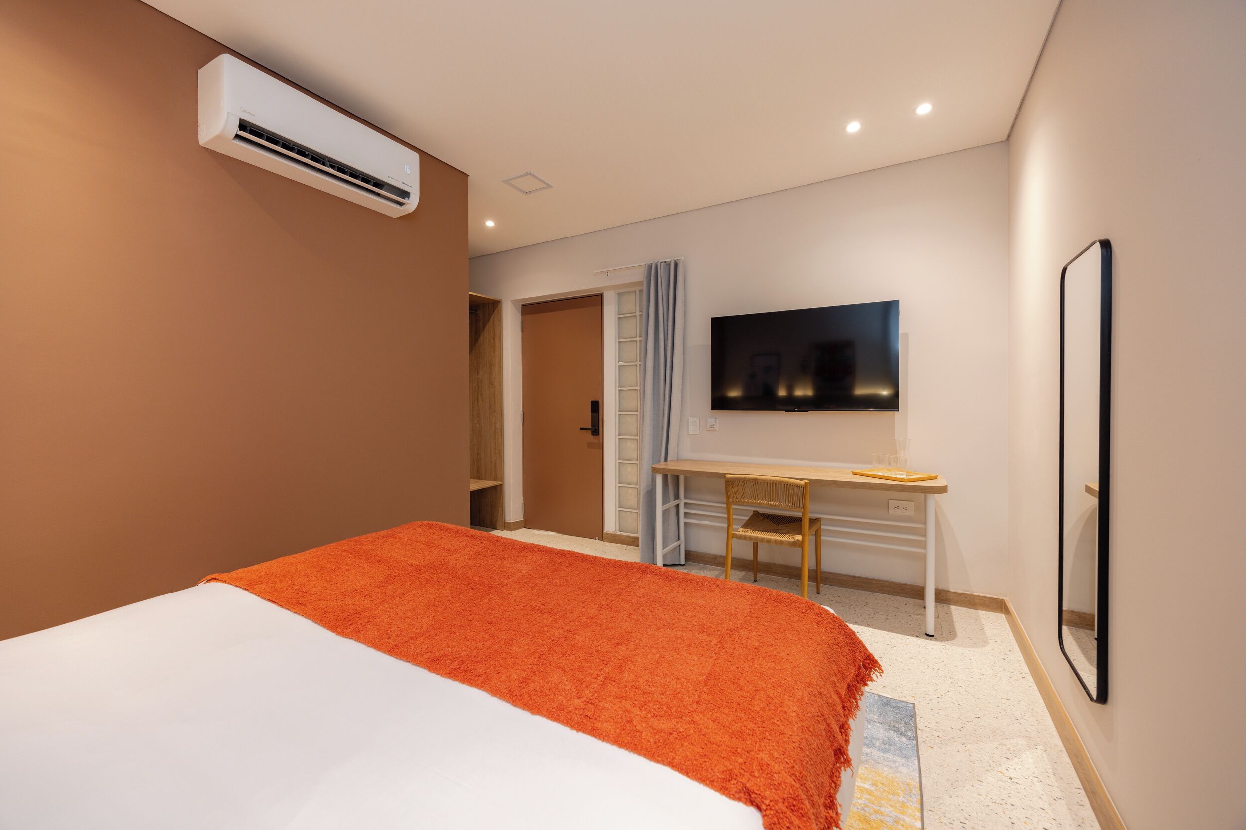A hotel room with a bed, a desk, a TV, and an air conditioning unit.