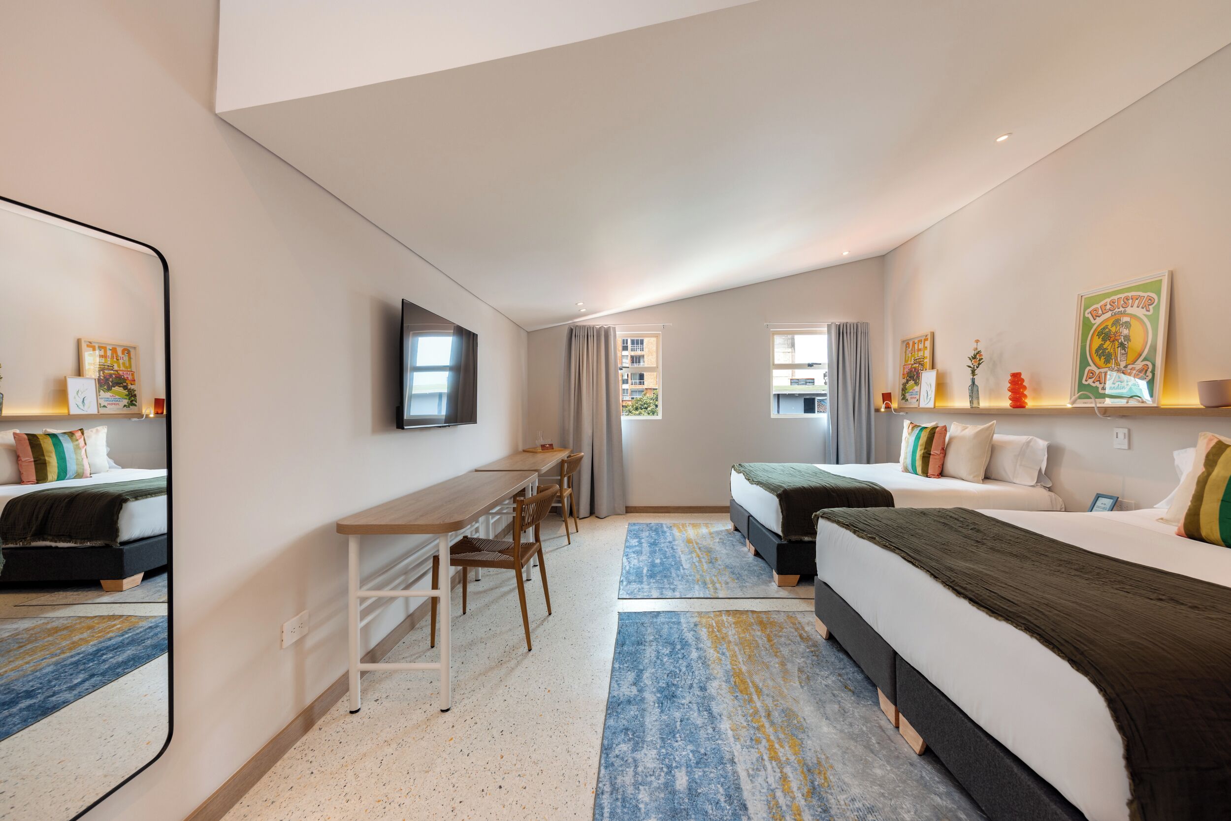 Une chambre d’hôtel moderne équipée d’un lit, d’un bureau, d’une chaise et d’un grand miroir.