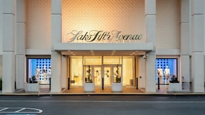 The entrance of Saks Fifth Avenue with a large glass facade and potted plants at the entrance.