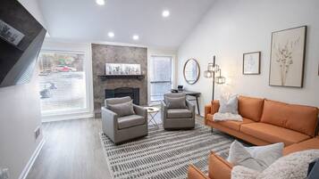 Un salon moderne avec une cheminée, deux fauteuils, un canapé et un tapis à motifs.