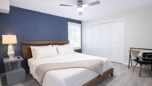 Un dormitorio con cama, mesita de noche, lámpara, silla y ventilador de techo.