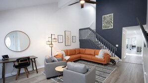 Una sala de estar moderna con un sofá modular, un espejo redondo, un escritorio y una escalera.