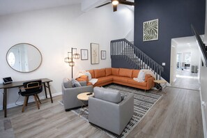 A modern living room with a sectional sofa, a round mirror, a desk, and a staircase. - Sandy Springs Spacious 3 Bedroom, 2 Bath | 2 King Beds | Central Location (Atlanta)