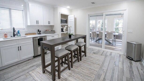 Una cocina moderna con armarios blancos, una isla central con taburetes, un microondas y vistas a un patio exterior a través de puertas de vidrio.