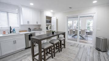Une cuisine moderne avec des meubles blancs, un îlot central doté de tabourets, un four à micro-ondes et une vue sur une terrasse extérieure, accessible par des portes vitrées.