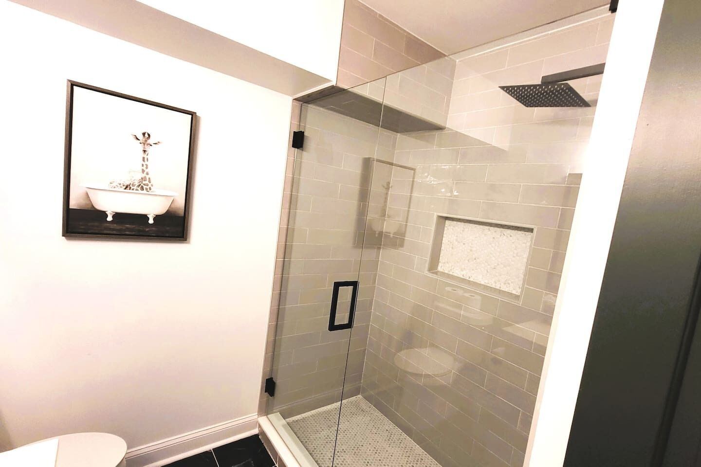 A modern bathroom with a glass shower enclosure, a framed picture on the wall, and a white bathtub.