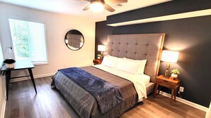A modern bedroom with a large bed, a ceiling fan, a bedside table with a lamp, and a wall-mounted mirror. - 7 BR / 5 BA | 2 Homes Sandy Springs Near Buckhead (Atlanta)