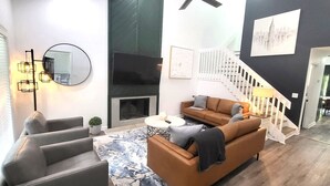 A modern living room with a fireplace, a sofa, a coffee table, and a staircase. - 7 BR / 5 BA | 2 Homes Sandy Springs Near Buckhead (Atlanta)