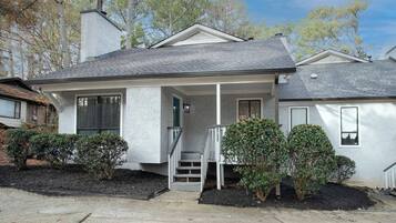 A single-story house with a front porch, a chimney, and a small front yard with shrubs.