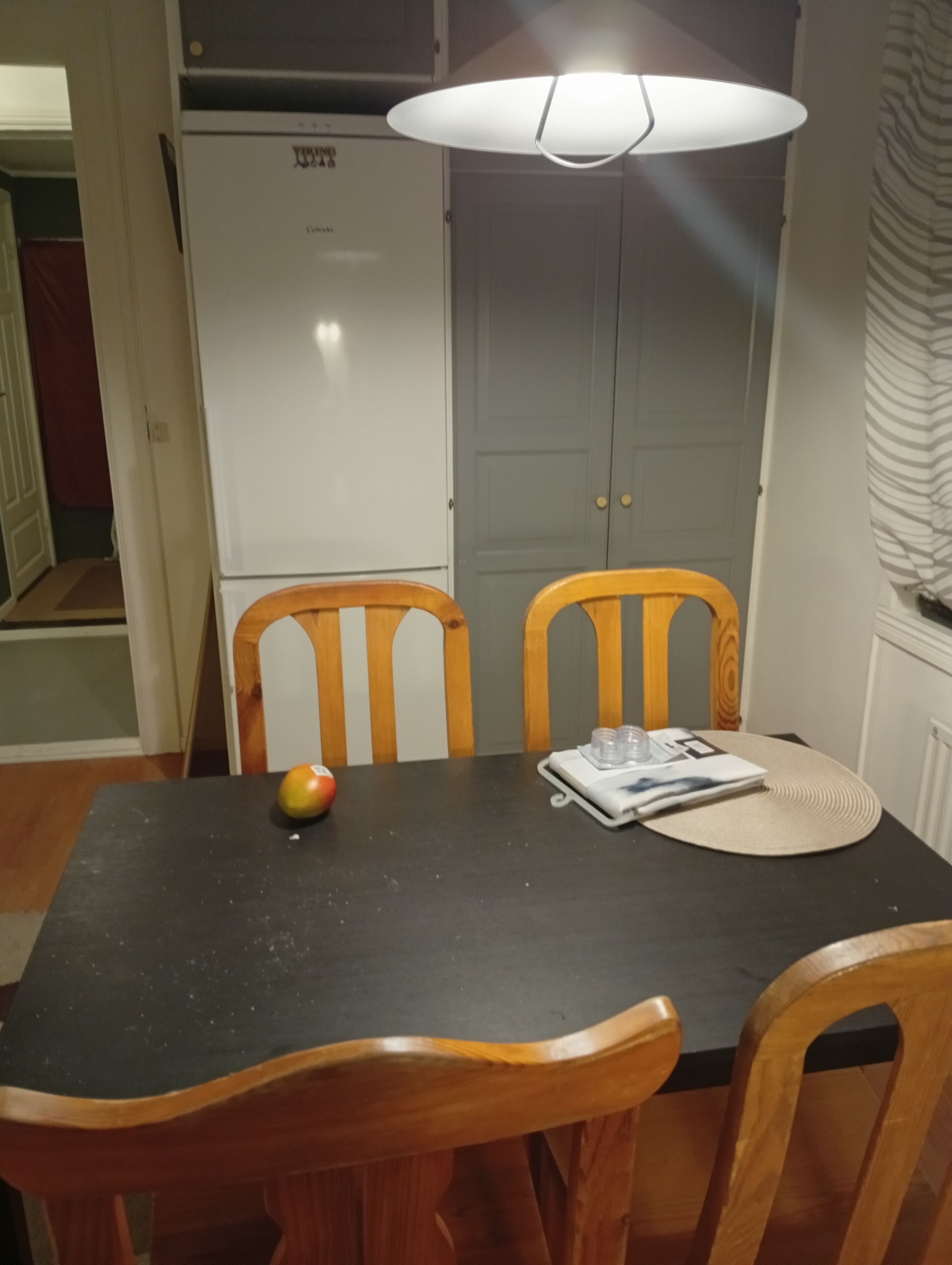 Ein Essbereich mit Tisch, zwei Holzstühlen, einem weißen Kühlschrank und einer Deckenleuchte.