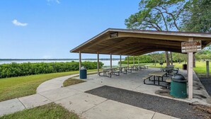 Een overdekte picknickplaats met banken en picknicktafels, een vuilnisbak en een bord dat reserveringstijden voor parkeerplaatsen aangeeft.